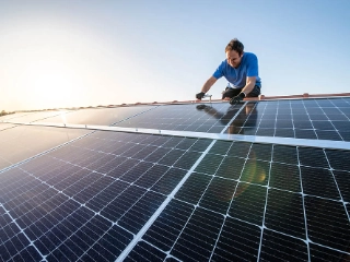 Mann installiert auf einem Dach eines Eigenheims eine Photovoltaikanlage. 